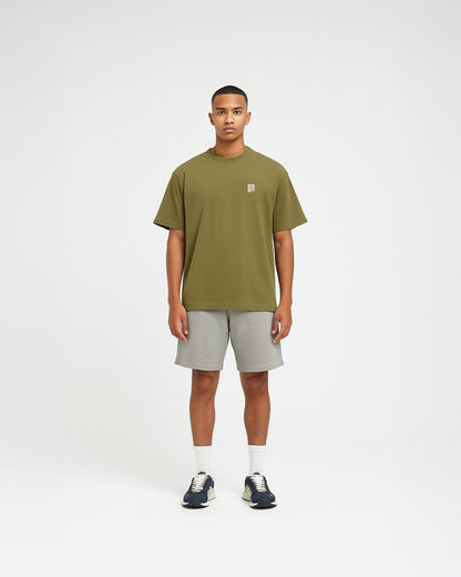 Model draagt een olijfgroen oversized T-shirt van 1cultuur met op de borst de quote “Sta weer op” in kleine witte letters, streetwear geïnspireerd design.